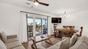 A living room with a sofa, a coffee table, and a dining table with chairs. There is a TV mounted on the wall and a ceiling fan. - Gulf Side in Seagrove Beach, Awesome Location + Free Attraction Tickets! (Santa Rosa Beach)