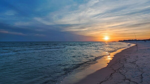 A beach with a sunset, calm sea, and a fishing rod on the sand.