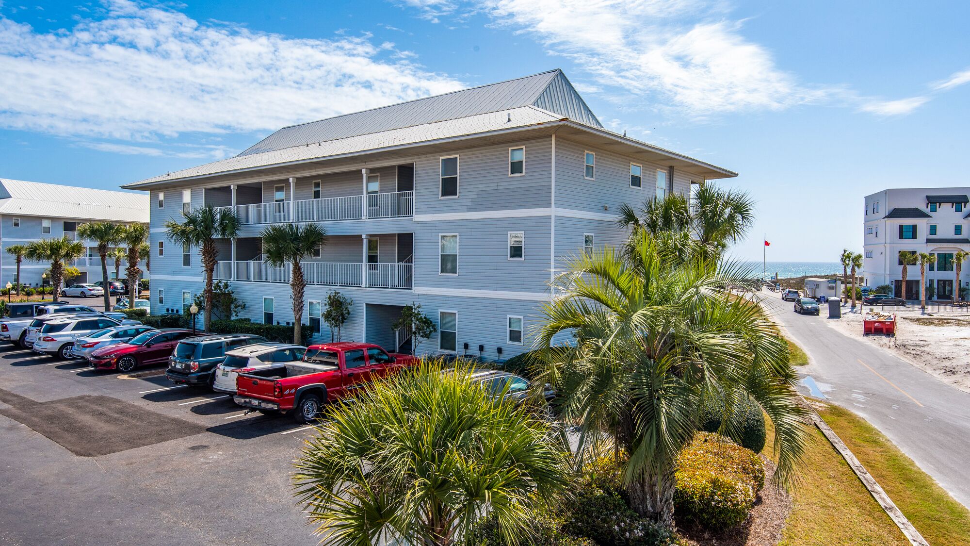 Un hôtel à plusieurs étages doté d’un parking, offrant une vue sur la plage et bordé de palmiers.