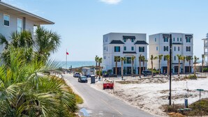 A coastal road with modern buildings, palm trees, and a clear view of the sea.