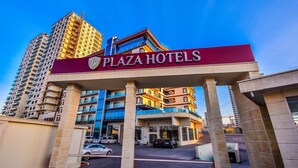 Entrada do Plaza Hotels com design arquitetônico moderno, com uma placa de destaque e área de estacionamento.