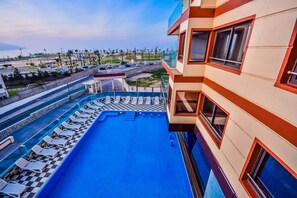 A rooftop pool with lounge chairs, a view of the surrounding area, and a building with balconies.