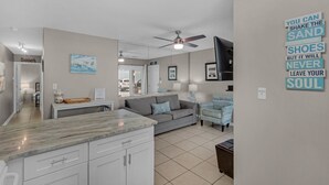 A modern living room with a grey sofa, a patterned armchair, a marble kitchen island, and a ceiling fan. - 2 Pools, Beach Access, Tennis, Family Friendly + Free Attraction Tickets! (Santa Rosa Beach)