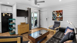 Ein modernes Wohnzimmer mit einer Couch, einem Couchtisch, einem Fernseher und einem Balkon mit Gartenmöbeln.