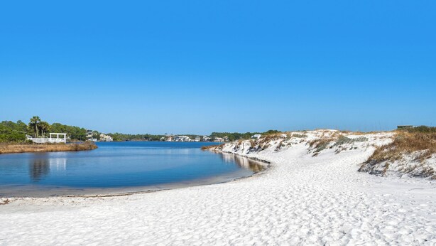 Una playa con orilla arenosa, una masa de agua tranquila y un pabellón blanco.