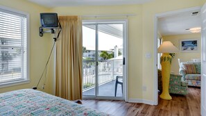 A room with a bed, a television mounted on the wall, a balcony with a chair, and a lamp. - Steps from the Gulf ~ 2 Community Pools ~ Tennis + Free Attraction Tickets! (Santa Rosa Beach)