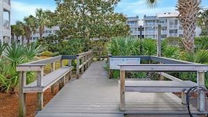 A wooden boardwalk leading to a building with a 'NOTICE: NO SQUARE CANOPIES PERMITTED ON THE BEACH' sign.
