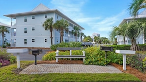 A multi-story building with a flat roof, surrounded by palm trees and a paved walkway.
