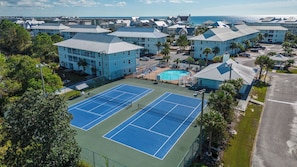 A coastal hotel with multiple tennis courts, a swimming pool, and a view of the ocean.