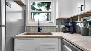 A kitchen with white cabinets, a herringbone tile backsplash, a window with a view of palm trees, a sink, and a coffee maker. - Ground Floor, 2 Pools, Tennis, Beautiful Community + Free Attraction Tickets! (Santa Rosa Beach)