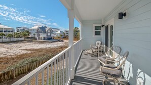 Een huis aan de kust met een veranda, rieten stoelen en uitzicht op het strand en omliggende huizen.