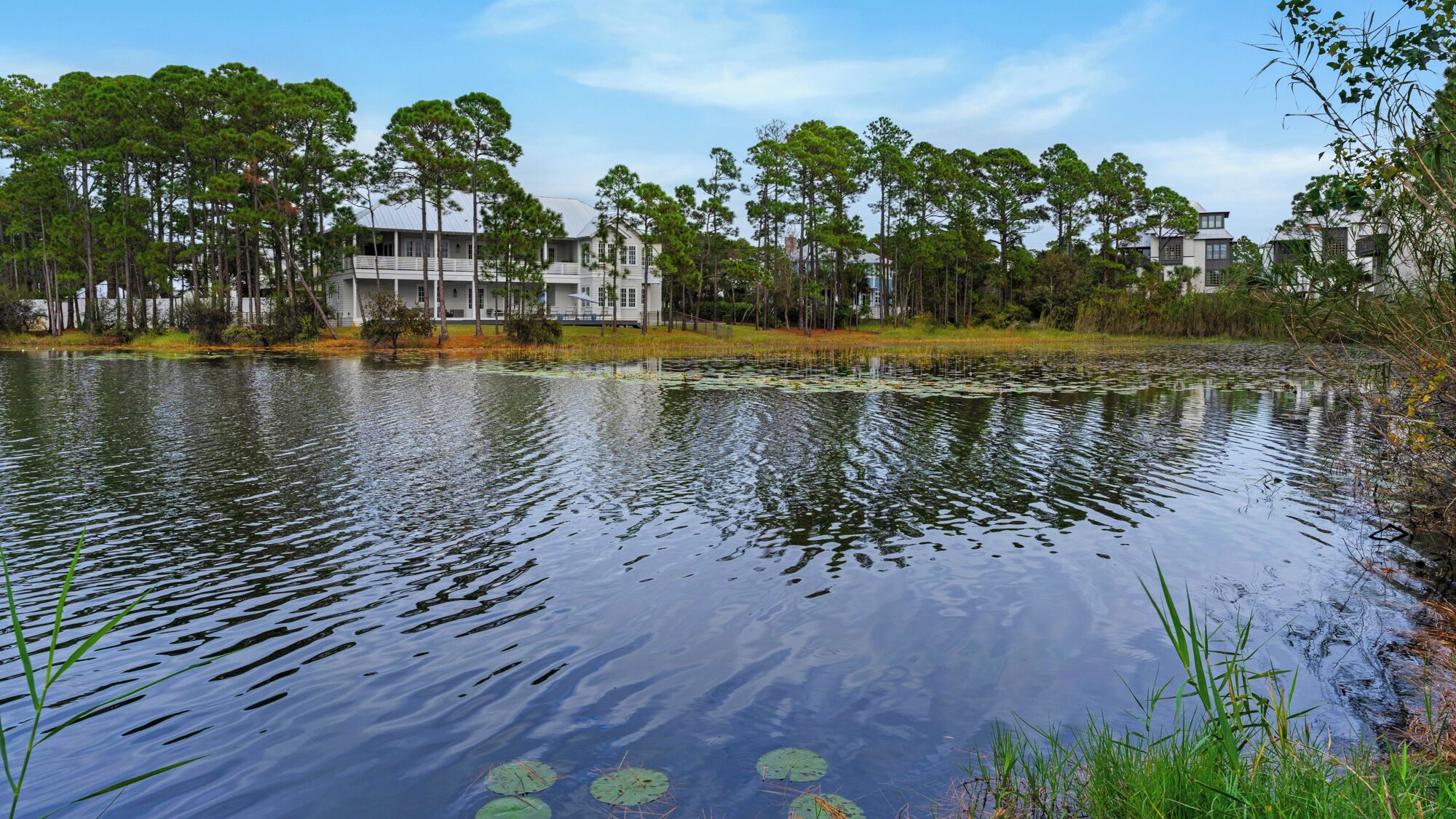 A calm lake with a reflection of buildings and trees, surrounded by greenery.