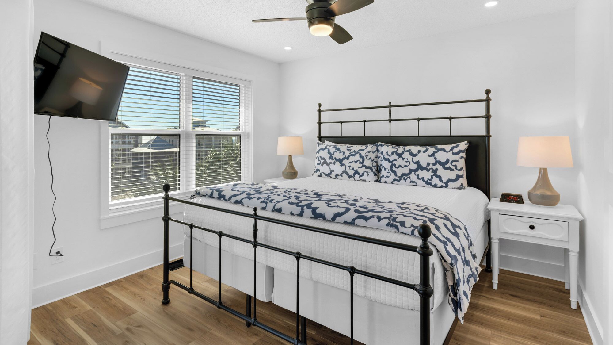 A bedroom with a bed, bedside tables, a TV mounted on the wall, and a ceiling fan.