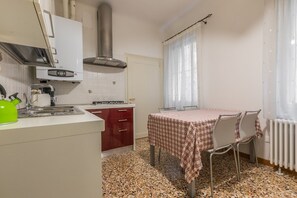 A compact kitchen with a gas stove, a stainless steel range hood, and a red cabinet. There is a dining table with a checkered tablecloth and two chairs.