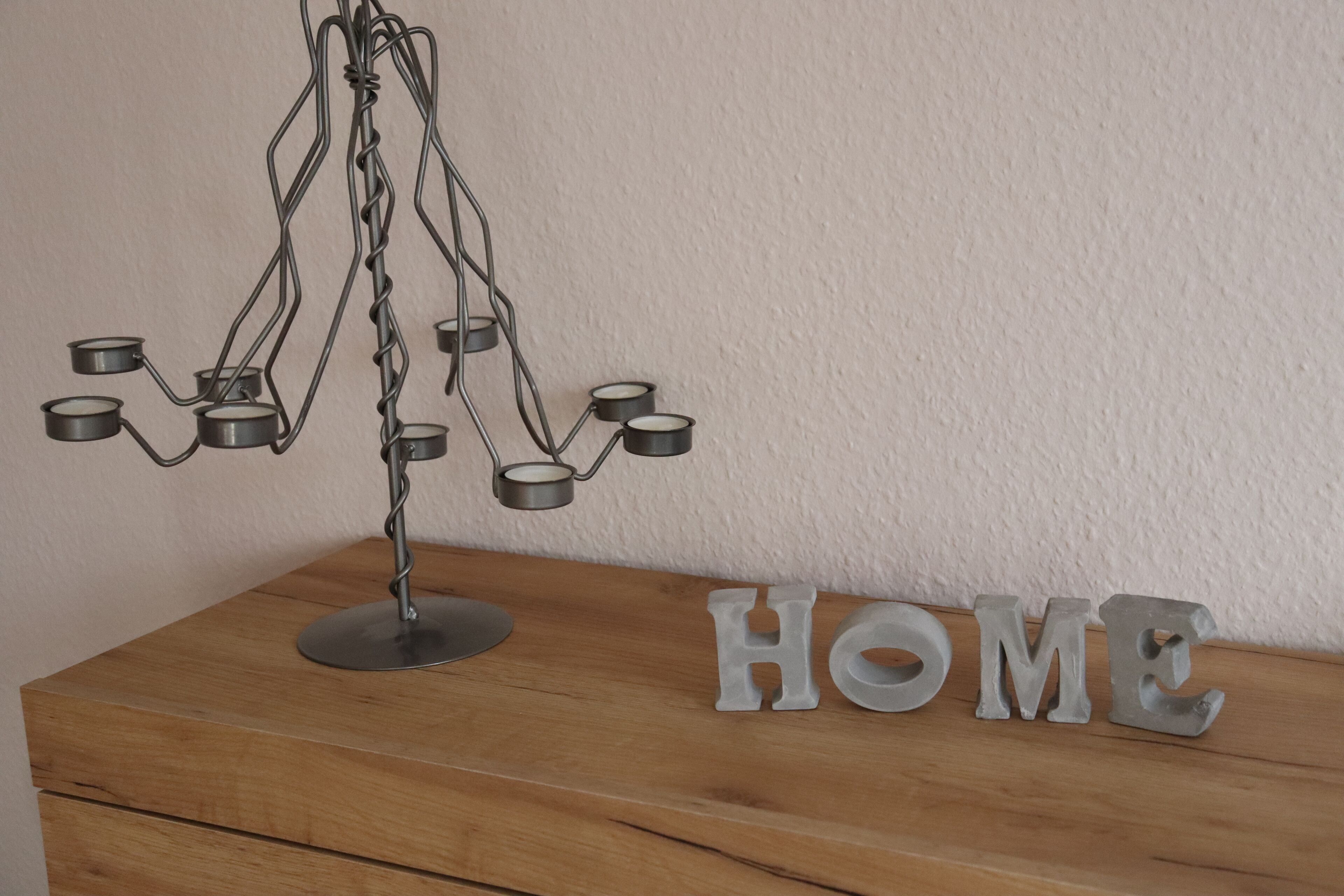 A metal candle holder with multiple candles on a wooden surface next to the word "HOME".