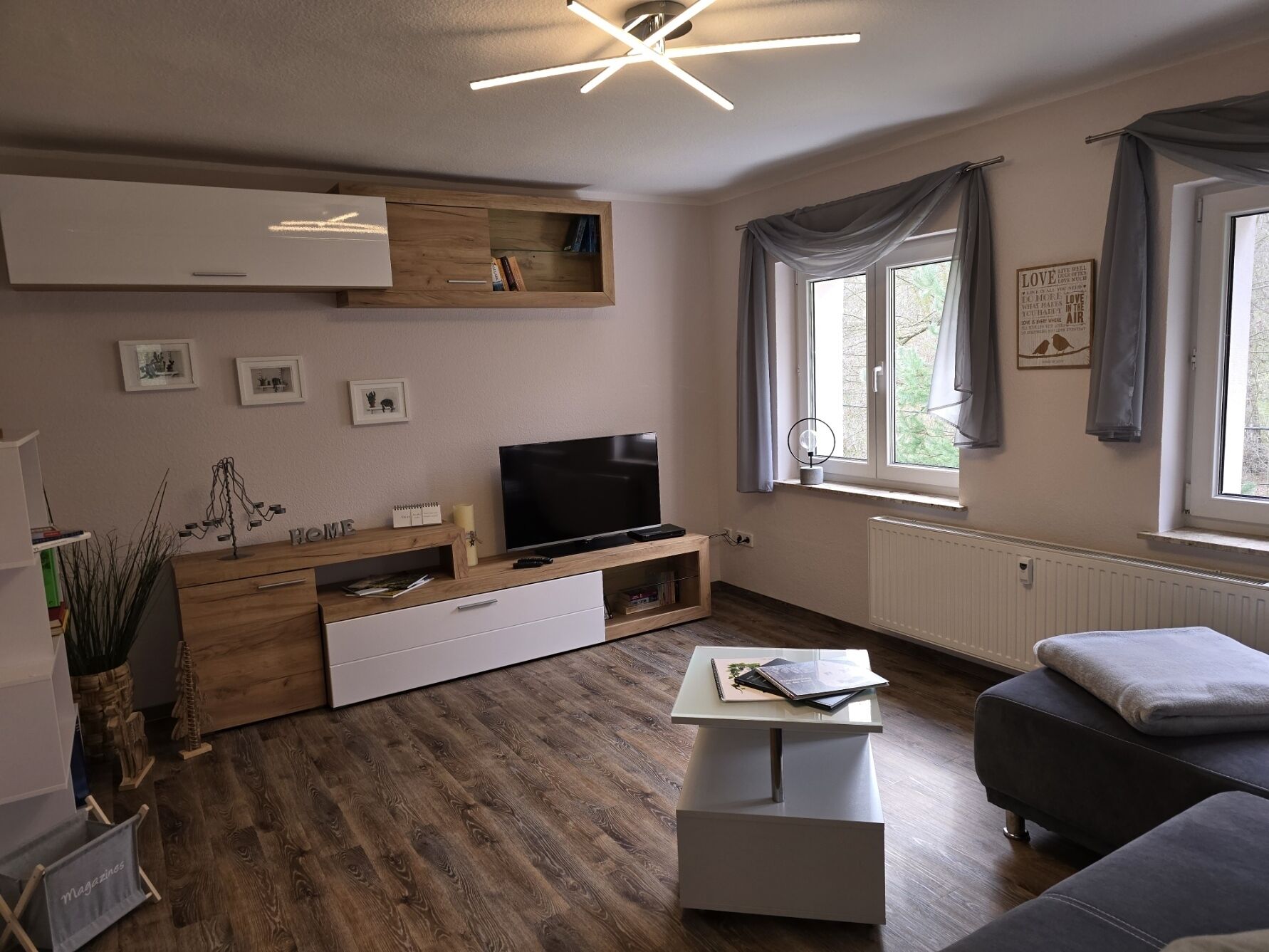 Un salon moderne avec un téléviseur à écran plat, des meubles en bois, une table basse blanche et un canapé gris.