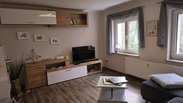 Un salon moderne avec un téléviseur à écran plat, des meubles en bois, une table basse blanche et un canapé gris.