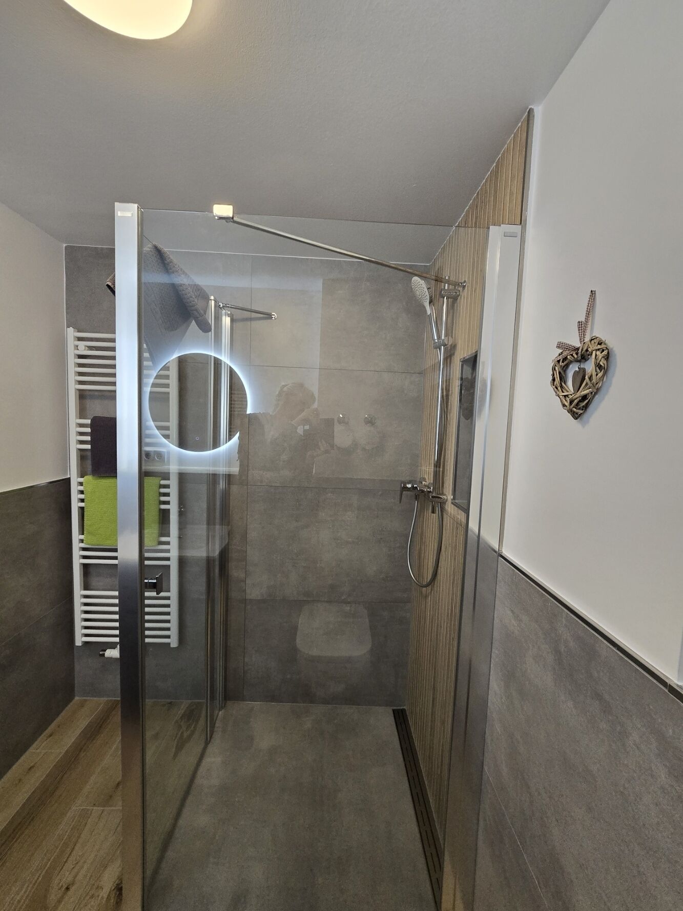 A modern shower area with a glass door, a towel rack, and a heart-shaped decoration on the wall.