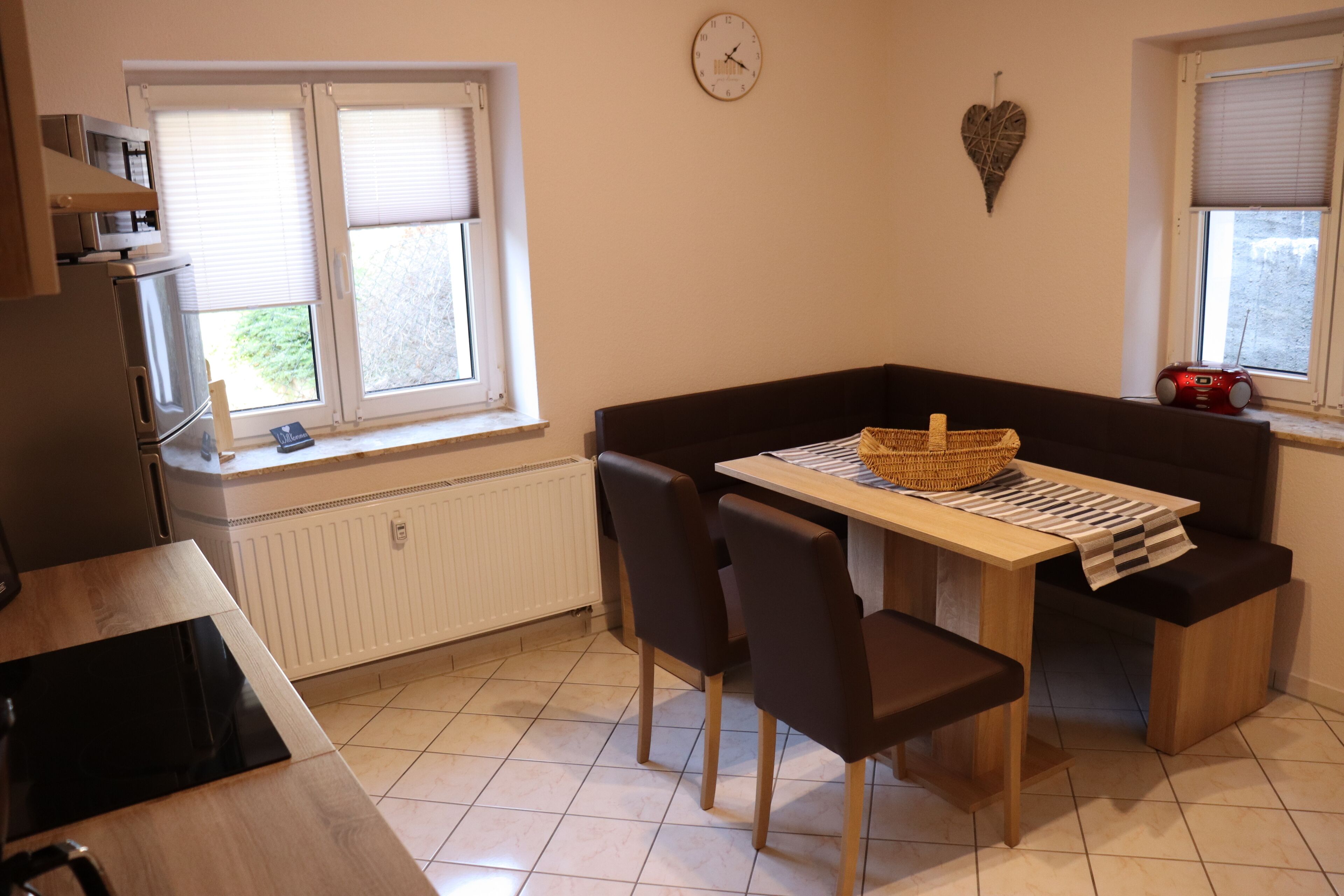 A compact kitchen with a dining area, including a table with chairs, a small refrigerator, and a window with blinds.
