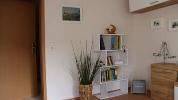 Ein Zimmer mit Holztür, einem Bücherregal mit Büchern, einer Pflanze und einem kleinen Schrank.