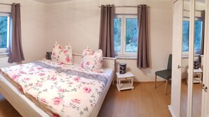 A bedroom with a bed, two windows with curtains, a bedside table, a chair, and a fan. - New apartment in the middle of vineyards (Coswig)