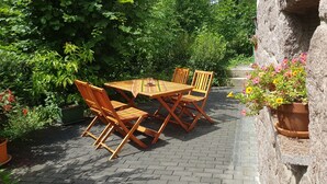 An outdoor patio with a wooden table and chairs, surrounded by potted plants and a stone wall. - New apartment in the middle of vineyards (Coswig)