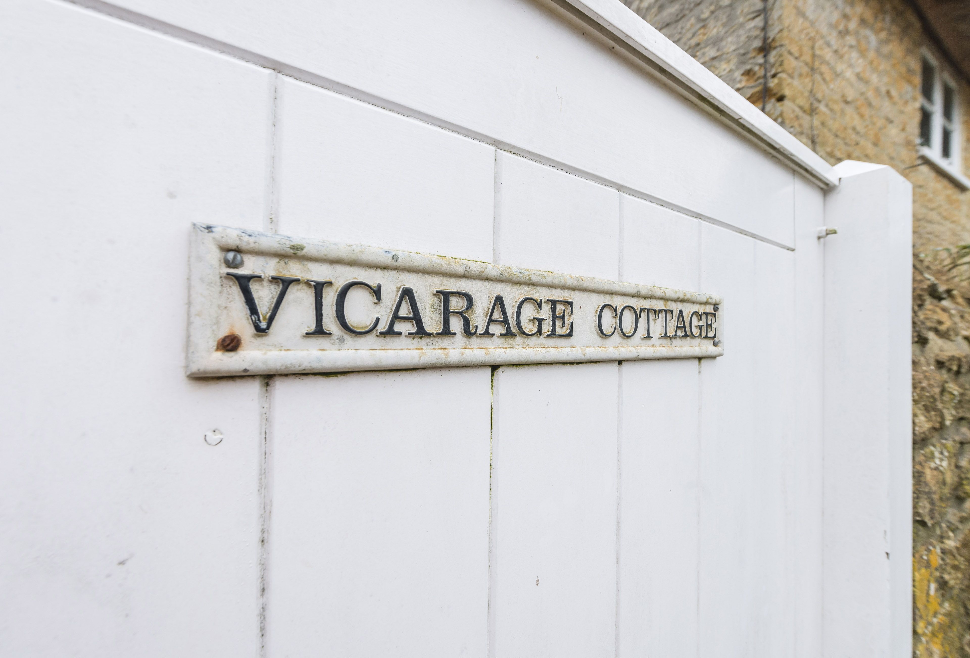 Un senyal de metall blanc amb el text 'VICARAGE COTTAGE' fixat a una paret blanca.
