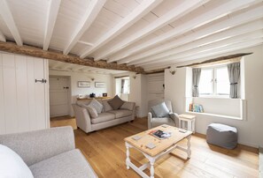 A cozy living room with a wooden ceiling, a sofa, a chair, a coffee table, and a window with curtains.