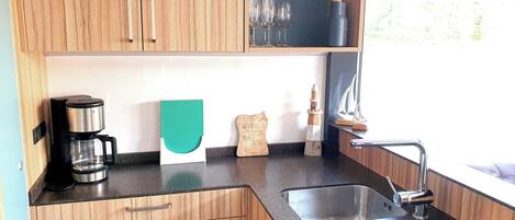 Una cocina con armarios de madera, una cafetera de acero inoxidable, una tabla de cortar verde, un letrero decorativo de madera y un grifo moderno.