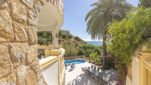 A stone wall with a pool and outdoor seating area, overlooking a coastal landscape. - Villa Ronda - Costa CarpeDiem (Calpe)