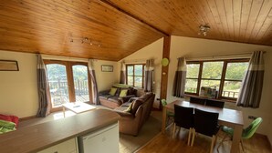 Una habitación acogedora con techo de madera, un sofá, una mesa de comedor con sillas y una pequeña cocina americana.