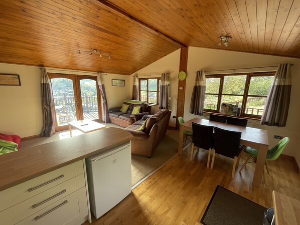 A cozy room with a wooden ceiling, a sofa, a dining table with chairs, and a small kitchenette.