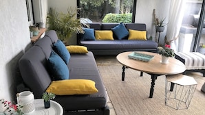 Una sala de estar moderna con un sofá gris oscuro, cojines amarillos y azules, una mesa de centro redonda de madera y una mesita auxiliar con una bandeja blanca.