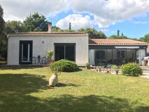 Ein modernes Haus mit Terrasse, kleinem Garten und einem großzügigen Zimmer mit Fenstern.