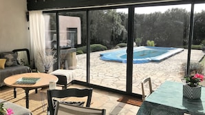 Un patio con mesa, sillas y vista a una piscina y jardín.
