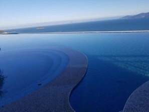 A clear view of a beach with a pier extending into the ocean, a curved pathway leading to the water, and a distant mountain range. - Luxury Scenia Bay Apartment with Seaview (Bac Nha Trang)