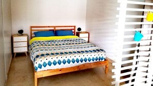 A bedroom with a wooden bed, two bedside tables, a white wall, and a white slatted partition. - Large studio in the center of Annecy (Annecy)