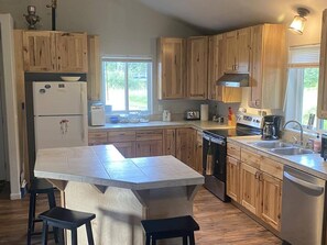 A kitchen with wooden cabinets, a large island with stools, a refrigerator, a dishwasher, and a window providing natural light.