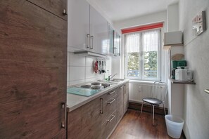 A modern kitchen with a wooden cabinet, a window with a red blind, a radiator, and a small stool.
