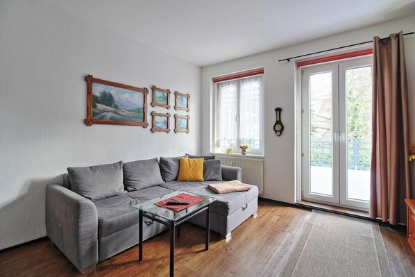 A living room with a grey sofa, a glass coffee table, and a wooden picture frame on the wall.