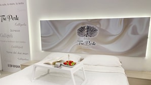 Un dormitorio ordenado con una cama blanca, una mesita de noche con un libro y un plato de fresas, y una obra de arte grande en la pared.