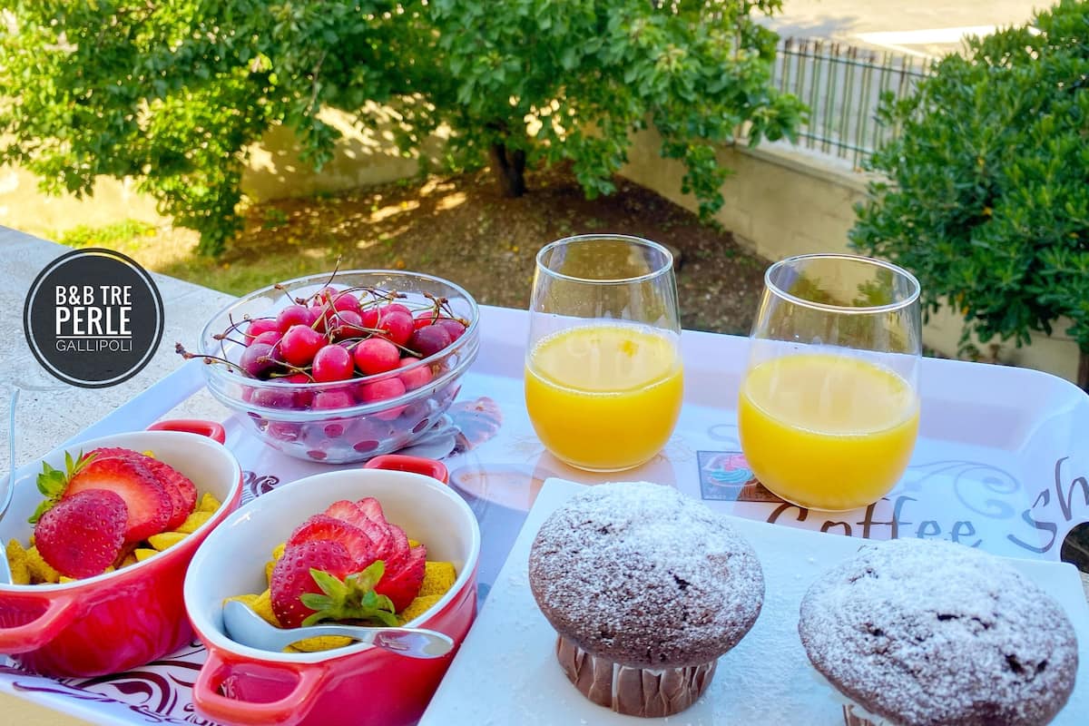 Una mesa de desayuno con un bol de cerezas, dos vasos de zumo de naranja, un muffin y un bol de fresas.
