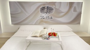 Una cama bien hecha con cabecera blanca, un libro abierto y una bandeja con fresas y una taza.