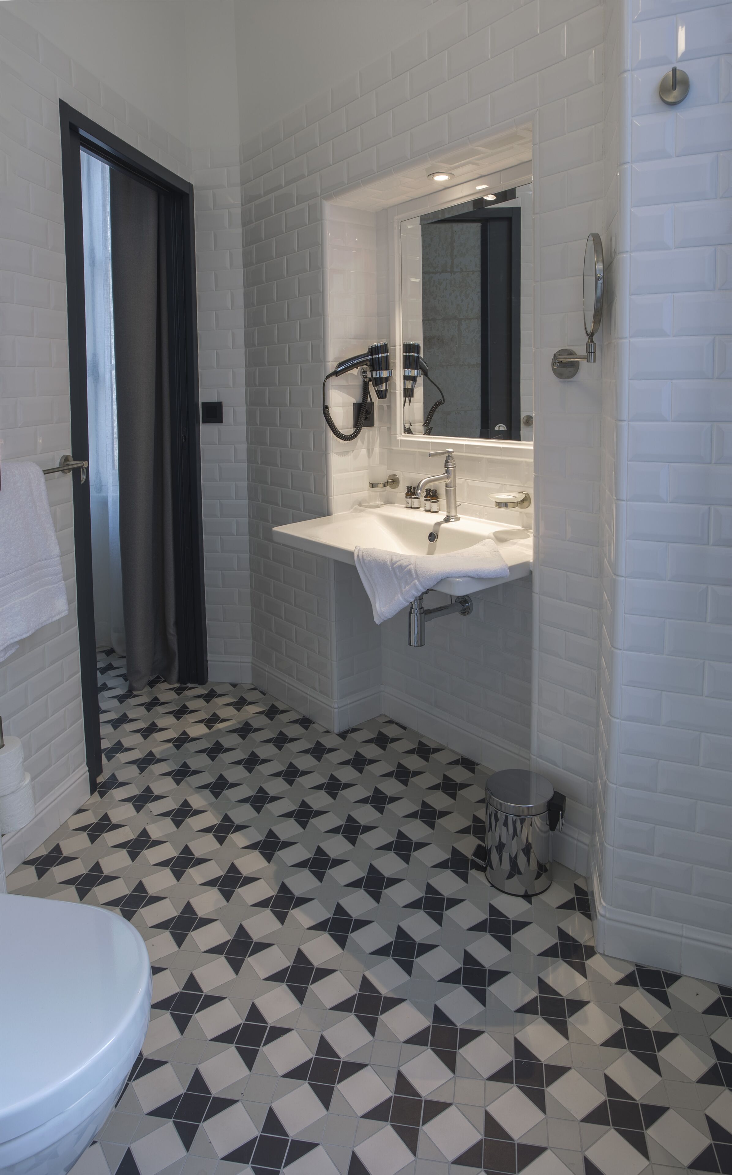 Un baño con lavamanos blanco, espejo y suelo con baldosas de diseño blanco y negro.