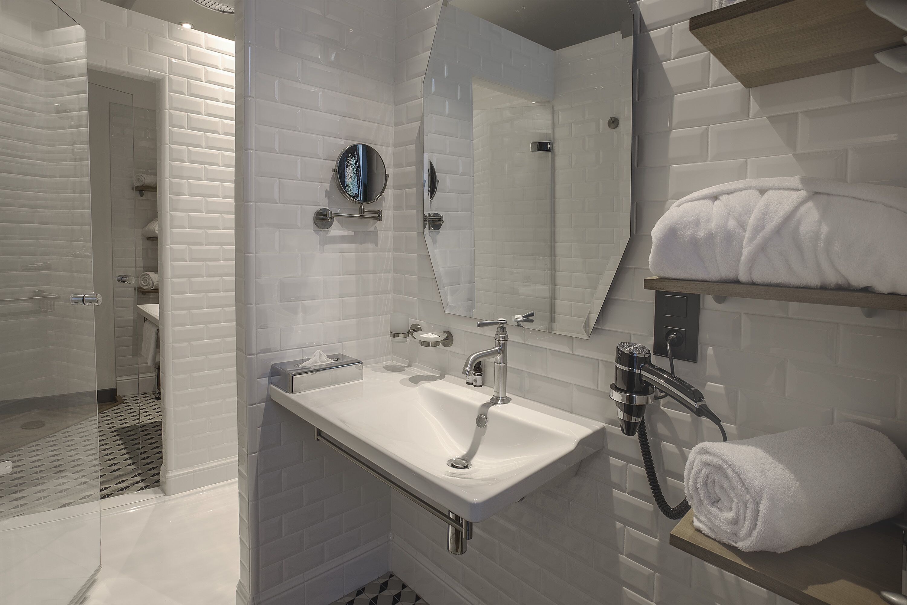 A modern bathroom with a white sink, a glass shower enclosure, and a towel on a shelf.