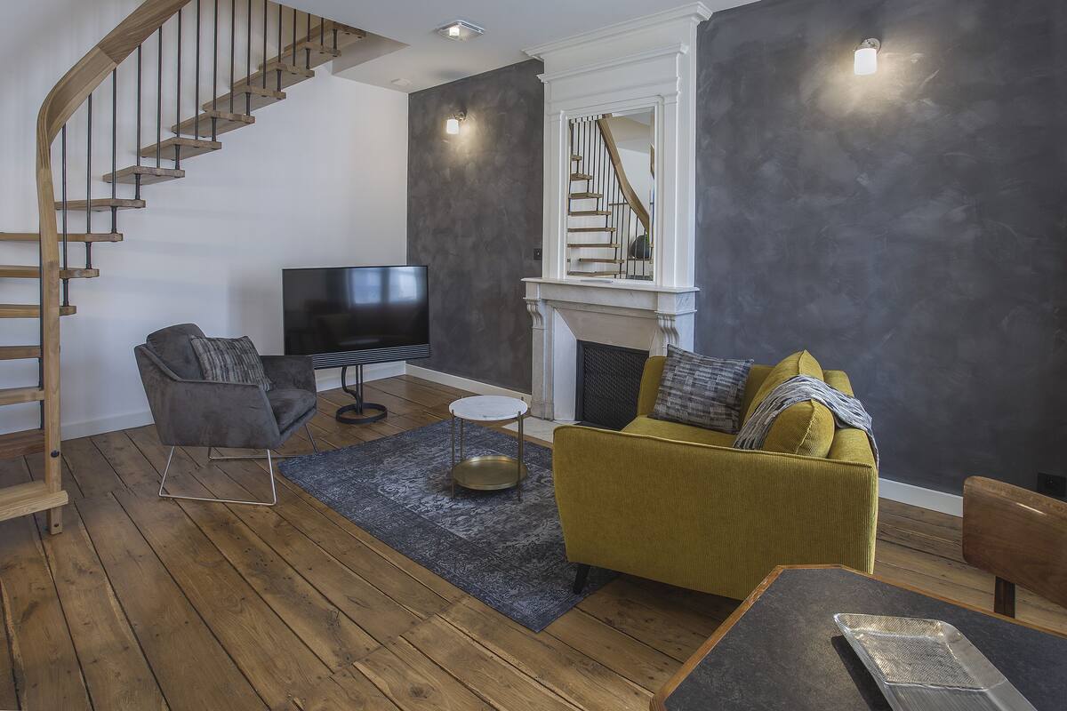 A living room with a wooden staircase, a sofa, a TV, and a fireplace.