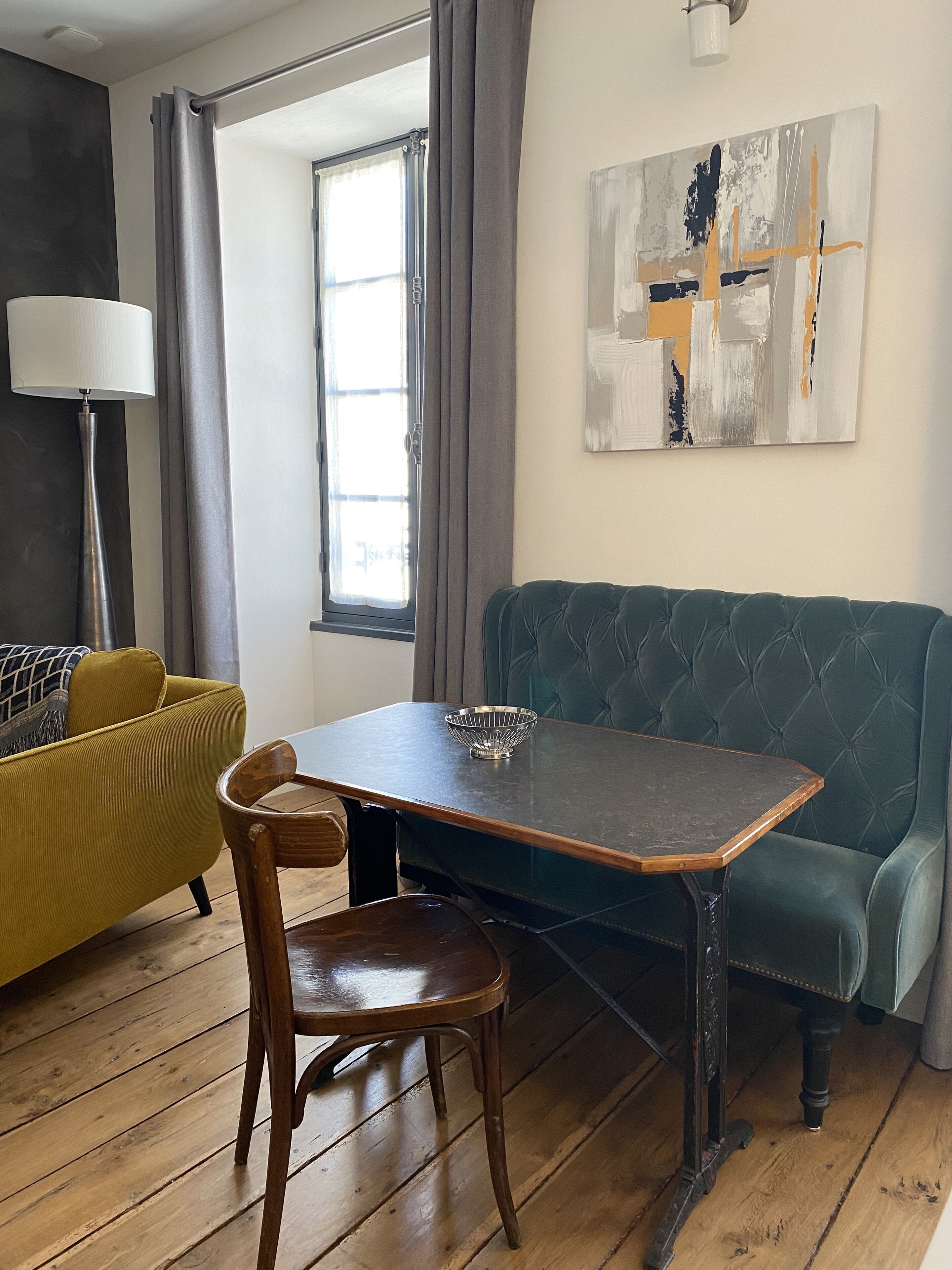 Un comedor con una mesa de madera, un sofá tapizado en verde y un sofá color mostaza, además de una lámpara de pie.