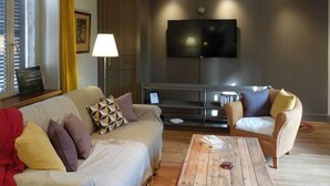 A living room with a sofa, armchairs, a coffee table, a TV, and a lamp.