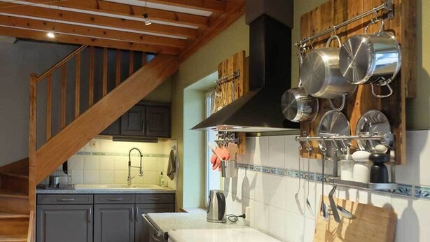 A kitchen with grey cabinets, a wooden staircase, and hanging pots.