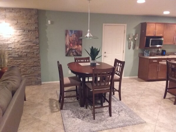 A dining area with a round table, four chairs, a potted plant, and a painting on the wall.